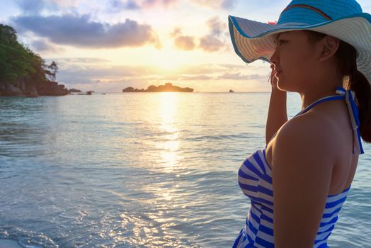 Girl with blue and white striped swimsuit standing watch nature sky and sea during the sunrise on beach of Honeymoon Bay at Koh Miang, Similan Islands National Park, Phang Nga, Thailand