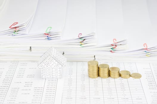 House and step pile of gold coins on finance account have step pile of paperwork as background.