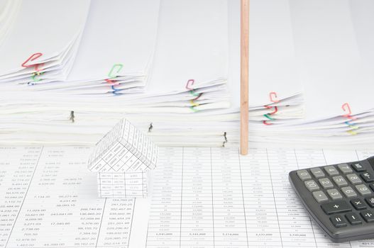 House and calculator on finance account have pencil place vertical with step pile of paperwork as background.