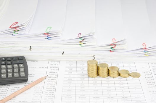 Pencil with calculator and step pile of gold coins on finance account have step pile of paperwork as background.