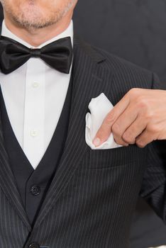 Close-up of a gentleman wearing Black Tie fixes his pocket square, vertical.