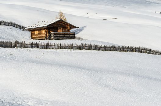 Traditional wooden log cabin with a fence in a white landscape consisting of snow.