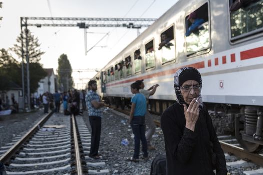 CROATIA, Tovarnik: An elderly refugee woman smokes at the railway station in Tovarnik, Croatia near the Serbian-border while police watch on in the background on September 18, 2015. Refugees are hoping to continue their journey to Germany and Northern Europe via Slovenia 