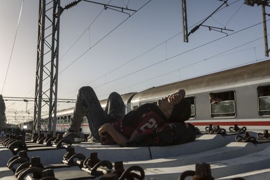 CROATIA, Tovarnik: A refugee lies down and rests at railway station in Tovarnik, Croatia near the Serbian-border while police watch on in the background on September 18, 2015. Refugees are hoping to continue their journey to Germany and Northern Europe via Slovenia 