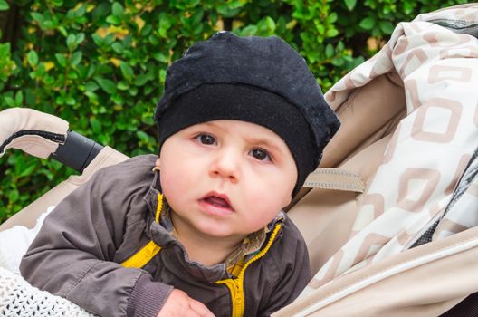 Baby with  cap sitting in a stroller, looking amazed. Background isolated.