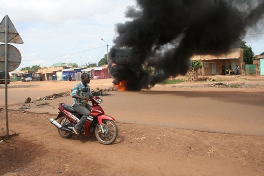 BURKINA FASO, Ouagadougou : A man on a motorcycle drives in front of a burning tire near the presidential palace in Ouagadougou, Burkina Faso, on September 18, 2015. Protests have sparked in Ouagadougou after Presidential guard officers seized power in a coup.