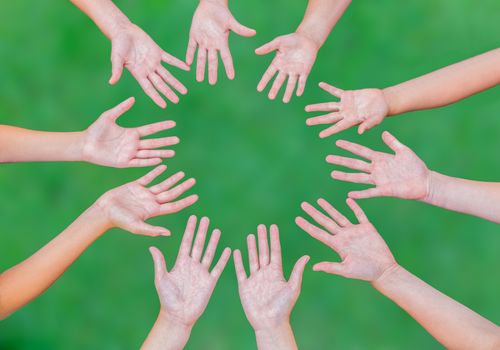 Arms of teens together in circle isolated on green grass fbackground