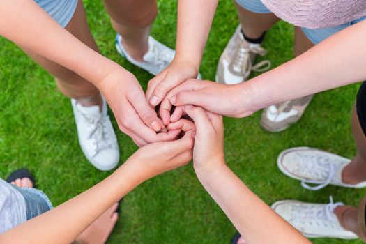 Five arms with hands of young girls entwined above green grass