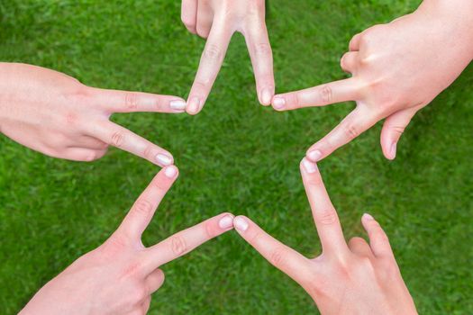 Five hands of teens making star shape together above grass