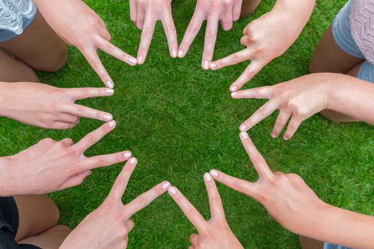 Many arms of girls with hands making ten pointed star above green grass