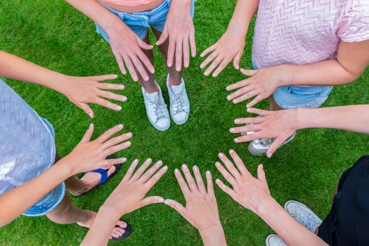 Many hands of young girls making circle above green grass