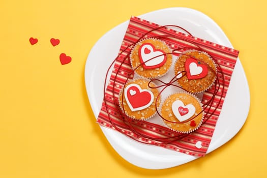 white plate with valentine's day muffins with red and white hearts isolated on a yellow background