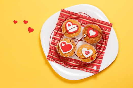 white plate with valentine's day muffins with red and white hearts isolated on a yellow background