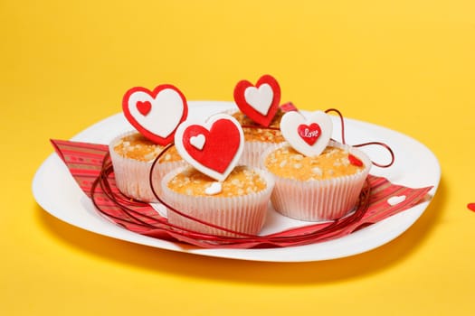 white plate with valentine's day muffins with red and white hearts isolated on a yellow background