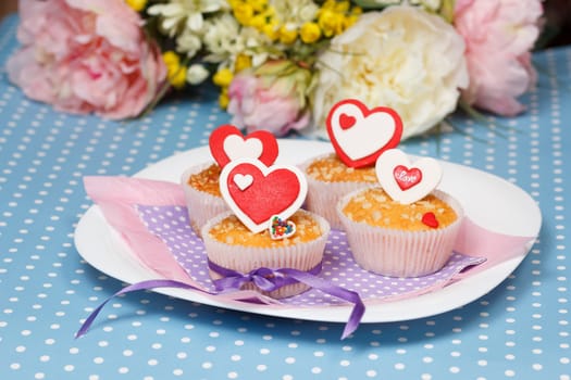 white plate with valentine's day muffins with red and white hearts on a blue with dots (polka dot) table and flowers on the background