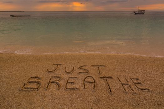 In the picture a beach at sunset with the words on the sand "Just breathe".