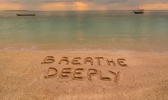 In the photo a beach in Zanzibar at sunset where there is an inscription on the sand "Breathe Deeeply".