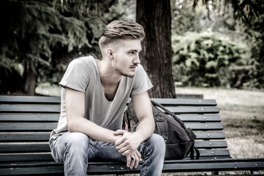 Handsome blond young man sitting on green, wooden park bench