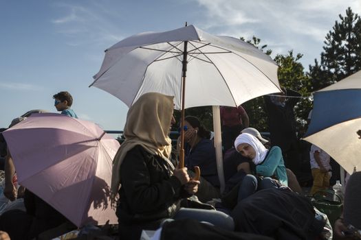 CROATIA, Harmica: Refugee shelter themselves from the sun with umbrellas on a bridge in the village of Harmica, Croatia on the border of Slovenia on September 19, 2015, after the Slovenian government blocked refugees from entering the country with riot police. Slovenia is the latest country to be forced into action over the global refugee crisis, with Slovenia's ambassador to Germany telling the Rheinische Post newspaper they will accept 'up to 10, 000' refugees