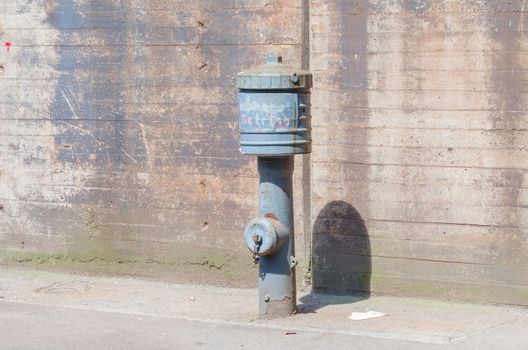 Nostalgic hydrant with drop jacket in front of a wall.