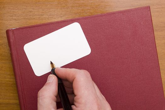 Businessman signs a business card, the hand of a man with fountain pen and red book.