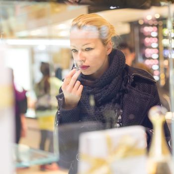 Beautiful blond lady testing and smelling perfume in a beauty store. Woman buying cosmetics in perfumery.