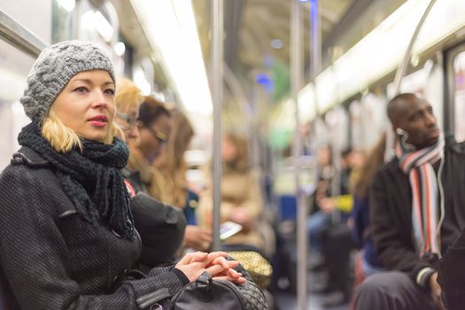 Beautiful blonde caucasian lady, wearing winter coat, traveling by metro in rush hour. Public transport.