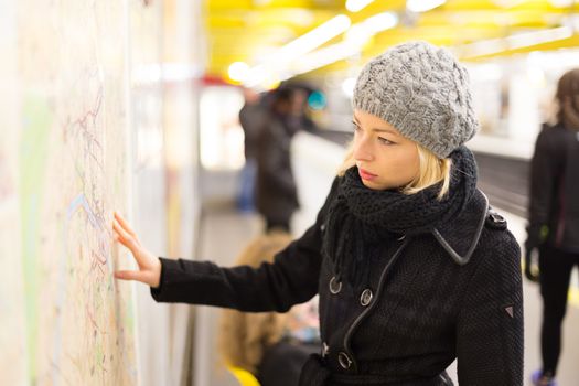 Casually dressed woman wearing winter coat, orientating herself with public transport map panel. Urban transport.