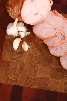 Ham slices on a wooden chopping board and garlic segments