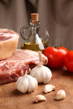 pieces of pork, garlic, tomato and vegetable oil on a chopping board