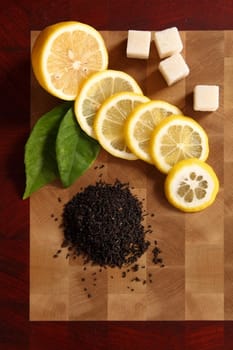 the cut lemon, sugar and black tea on a wooden chopping board