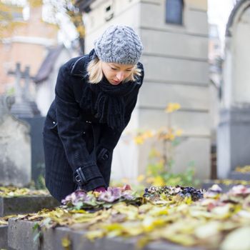 Solitary woman mourning with her hand on headstone, remembering dead relativesin on Pere Lachaise cemetery in Paris, France.