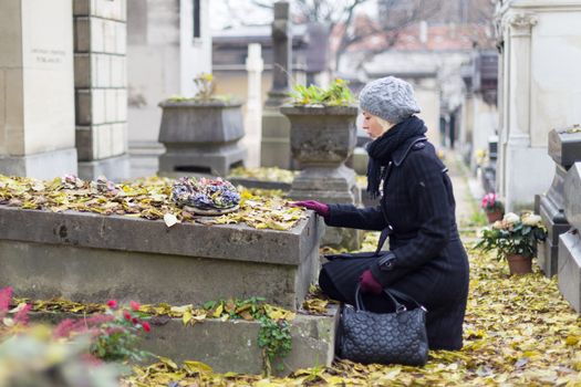 Solitary woman mourning with her hand on headstone, remembering dead relativesin on Pere Lachaise cemetery in Paris, France.