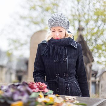 Solitary woman mourning with her hand on gravestone, remembering dead relativesin on Pere Lachaise cemetery in Paris, France.