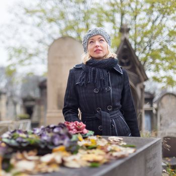 Solitary woman mourning with her hand on gravestone, remembering dead relatives in on Pere Lachaise cemetery in Paris, France.