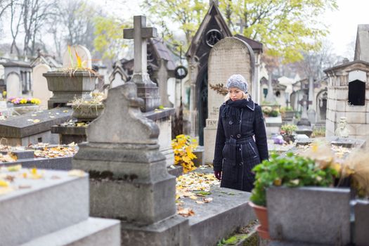 Solitary woman mourning by gravestone, remembering dead relatives in on Pere Lachaise cemetery in Paris, France.