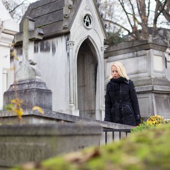 Solitary woman mourning by gravestone, remembering dead relatives in on Pere Lachaise cemetery in Paris, France.