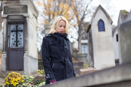 Solitary woman mourning by gravestone, remembering dead relatives in on Pere Lachaise cemetery in Paris, France.