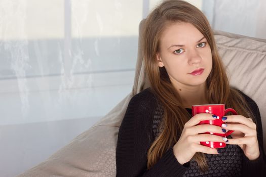 Young woman at home sitting on  chair in front of window  drinking coffee or tea