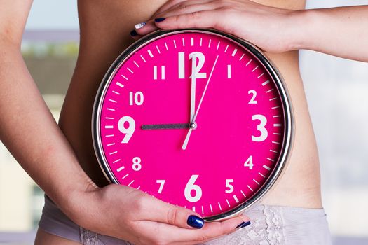 Biological clock ticking - woman holding clock in front of stomach. Pink clock in female hands