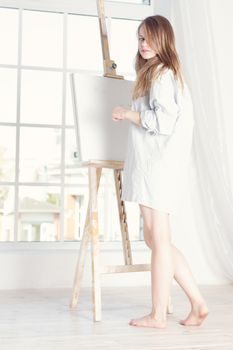 girl in a man's shirt near the easel. Houses near the window