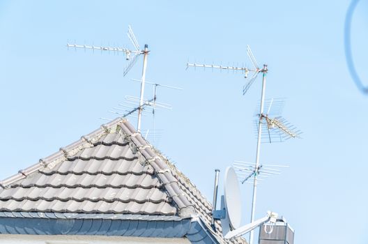 Distant view of a rooftop with many different TV antenna against a blue sky.