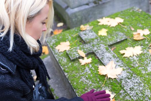 Solitary woman mourning with her hand on headstone, remembering dead relatives in on Pere Lachaise cemetery in Paris, France.