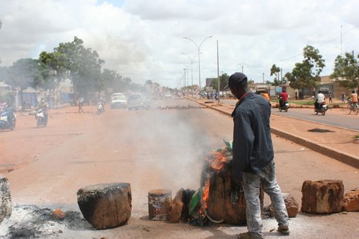 BURKINA FASO, Ouagadougou : A man gestures as he stands in front of burning tires on September 19, 2015 in Ouagadougou, Burkina Faso's capital. The protest comes several days after a military coup on September 16, by General Gilbert Diendere, an aide to ousted president Blaise Compaore and members of Compaore's powerful Presidential Security Regiment (RSP) burst into the cabinet meeting room snatching the country's interim president Michel Kafando and Prime Minister Isaac Zida, and two ministers (Augustin Loada and Rene Bagoro). Compaore was toppled October 2014 and fled into exile in Ivory Coast after a popular uprising triggered by his attempt to extend his 27-year rule. 