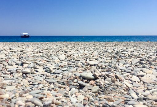 Detail of stones and sand in a desert beach with sea and a boat in the background