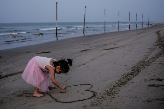 MALAYSIA, Kuala Terengganu:  A young girl draws a heart on the beach in Kuala Terengganu, Malaysia on September 21, 2015. Haze covered Malaysia for several days, but cleared on Monday morning. The country suffers from poor air quality and the haze often blankets the region. Malaysia and neighboring countries are trying to figure out a way to combat the haze which causes problems in the area.