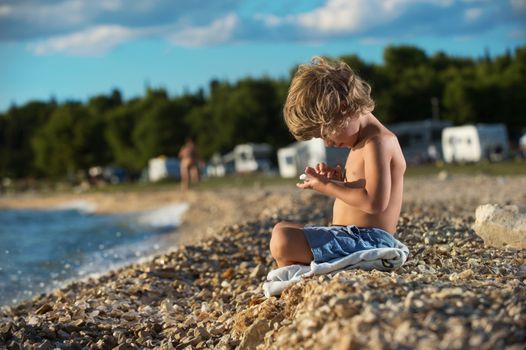 Cute little boy playing with his smart phone on the beach. Modern lifestyle, modern generation concept. Some negative space around.