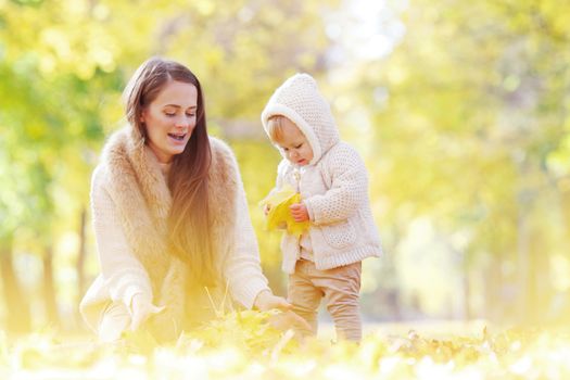 Mother and child having fun in autumn park among yellow leaves