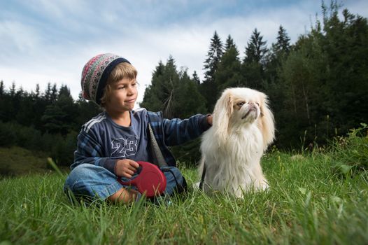 Cute little boy with a cap cuddling his dog in nature