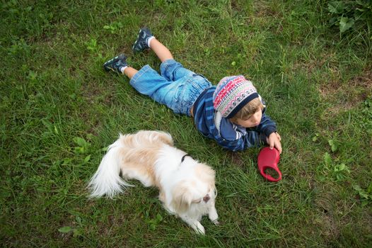 Little boy with a cap and his dog lying in the meadow.